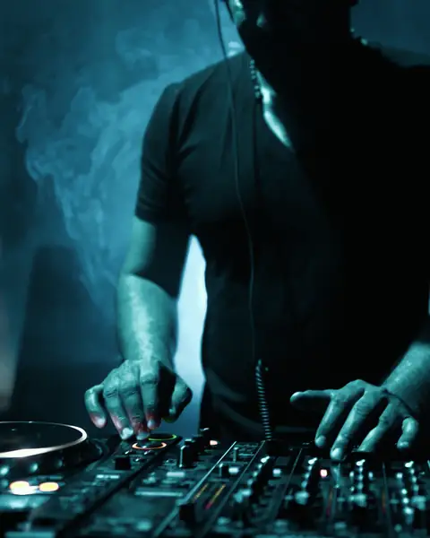 DJ mixing on a controller under blue studio lighting and haze